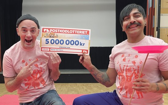 Två glada artister håller i en check på fem miljoner kronor