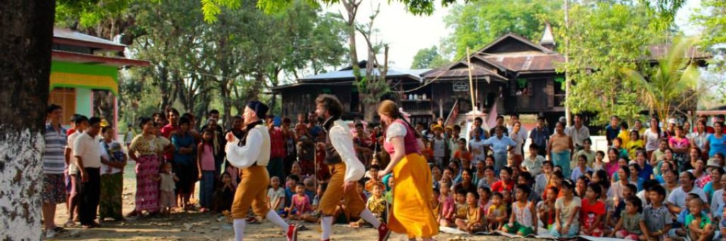 Clowner uppträder för publik i skydd av ett stort träd