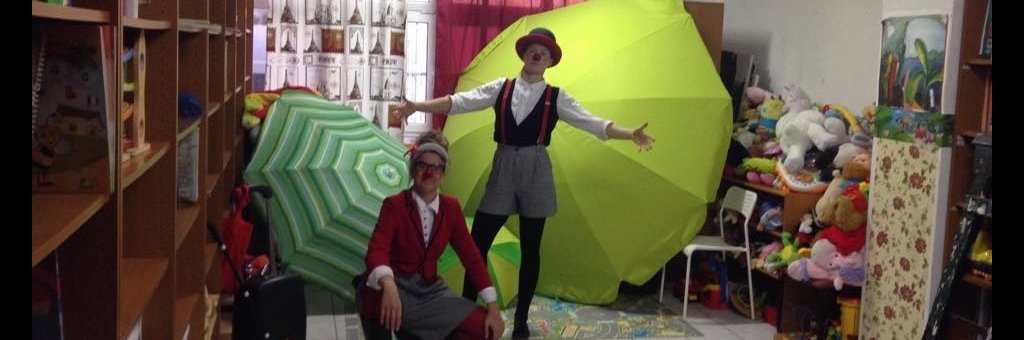 Två clowner poserar med gröna paraplyer i bakgrunden