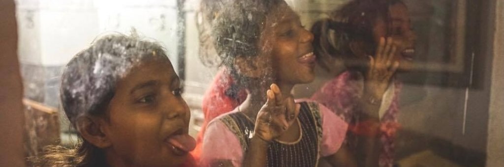 Tre flickor bakom en glasruta gör miner och skrattar