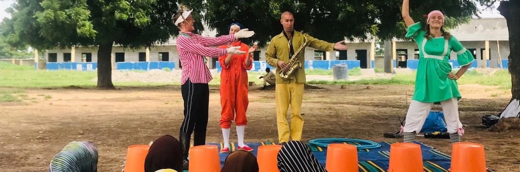 Fyra clowner i färgglada kläder uppträder för en grupp kvinnor i slöja