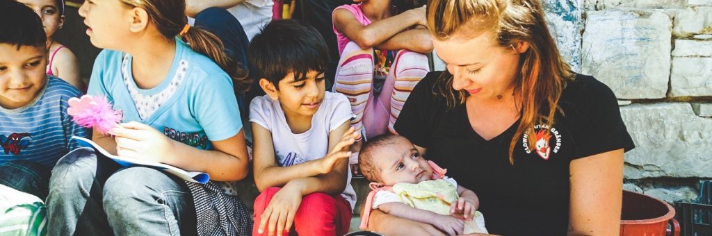 Kvinna sitter och håller ett barn i famnen omgiven av andra barn