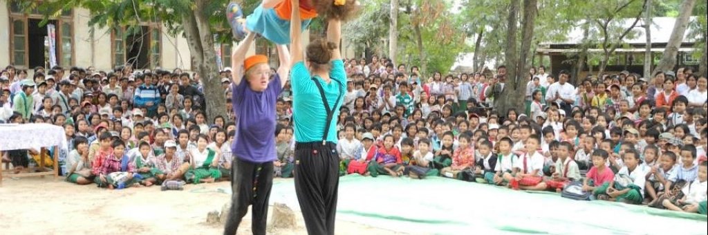 Två clowner balanserar en tredje över sina huvuden inför en stor publik