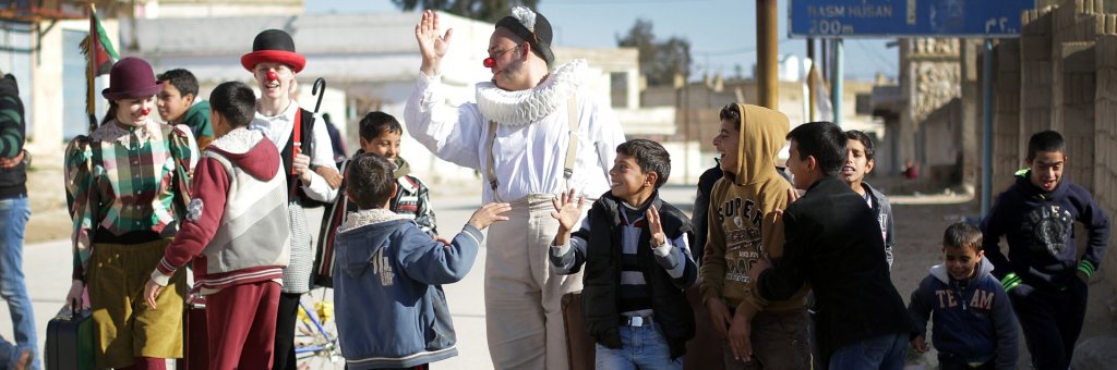Tre clowner promenerar på väg med en grupp barn