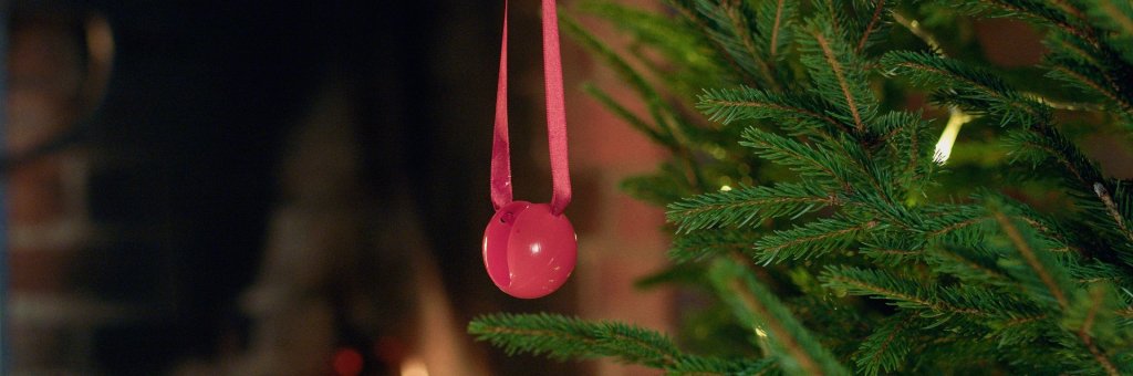 En röd clownnäsa hänger i rött band i en julgrand med ljus