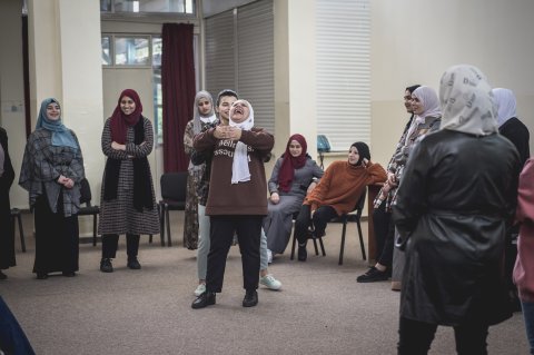 Kvinnor med hijab står i en ring, i mitten står två kvinnor och skrattar stort