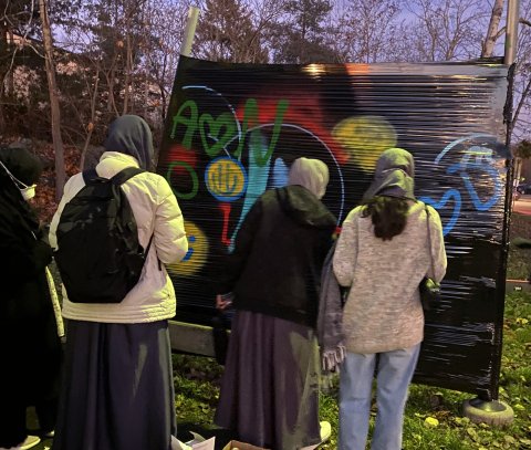 Tre unga tjejer målar graffiti på en stor målarvägg utomhus