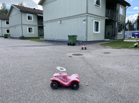 barns leksaker ligger utspridda på gårdsplanen framför gröna byggnader