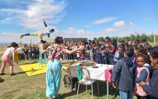 Artister uppträder med akrobatik för en stor grupp barn på en gräsplan. 