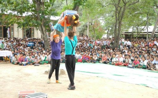 Två clowner balanserar en tredje över sina huvuden inför en stor publik