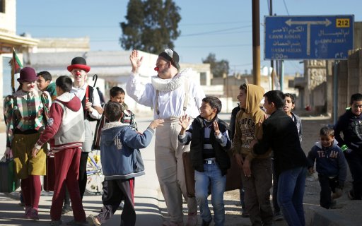 Tre clowner promenerar på väg med en grupp barn