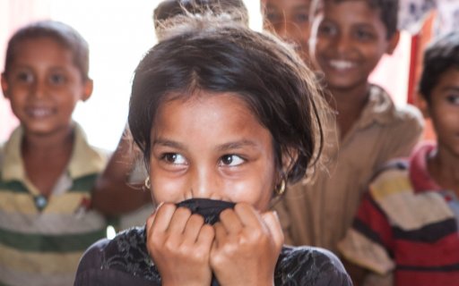 Närbild på flicka som ler och döljer munnen med sina händer