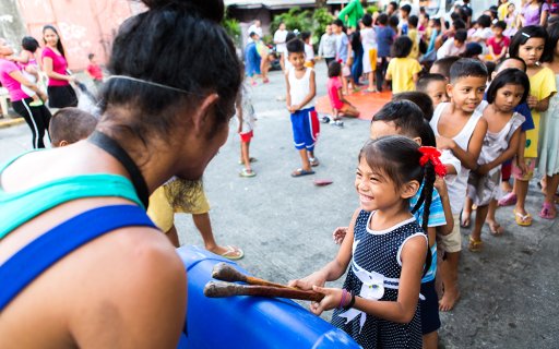 Flicka spelar på en hemgjord trumma av blå plast
